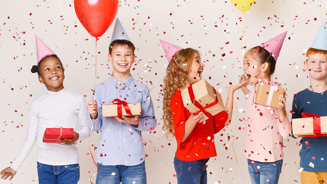 Kids celebrating birthday holding balloons and presents wearing birthday hats with confetti falling over white background