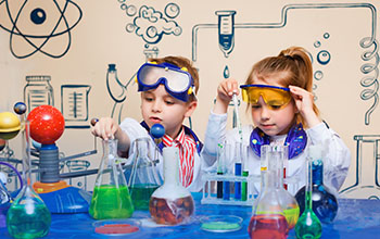 A boy and girl taking liquid from beaker using a pipette. On the table there are beakers and test tubes with colored liquids