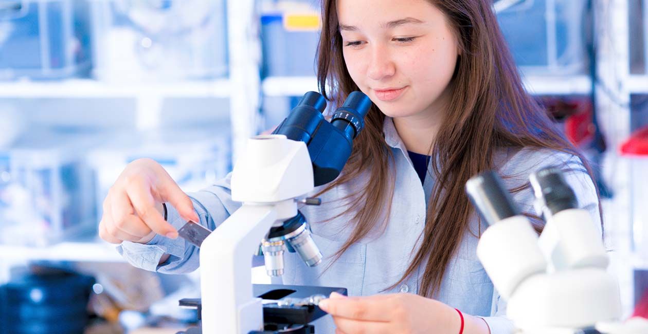 Girl in a lab coat looking at slides next to a microscope